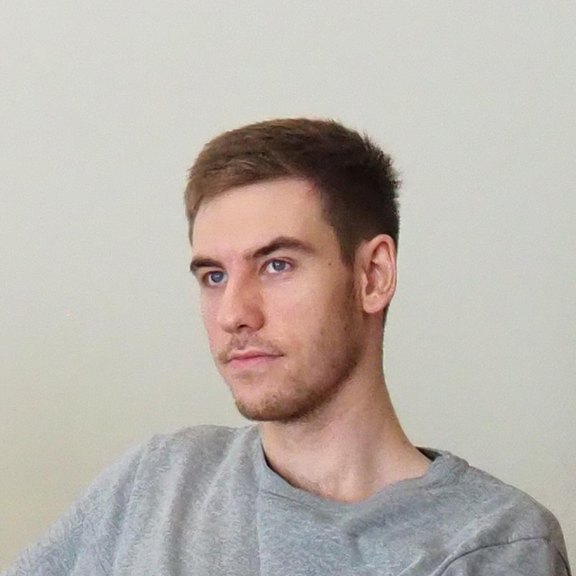 Timo Knoll mit grauem Pullover sitzend, neutraler Gesichtsausdruck