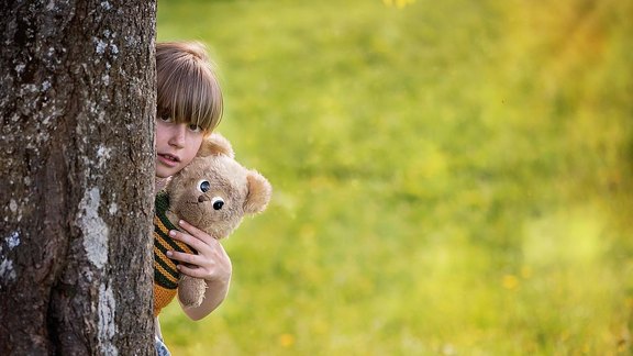 EJ Kinderschutz - Kind mit Plüschtier versteckt sich hinter Baum - Fotocredit: Pixabay
